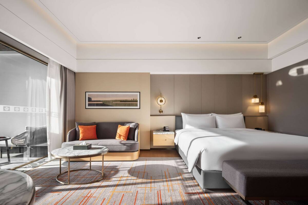 Una habitación de hotel moderna con una cama grande, un sofá, una mesita y un escritorio.