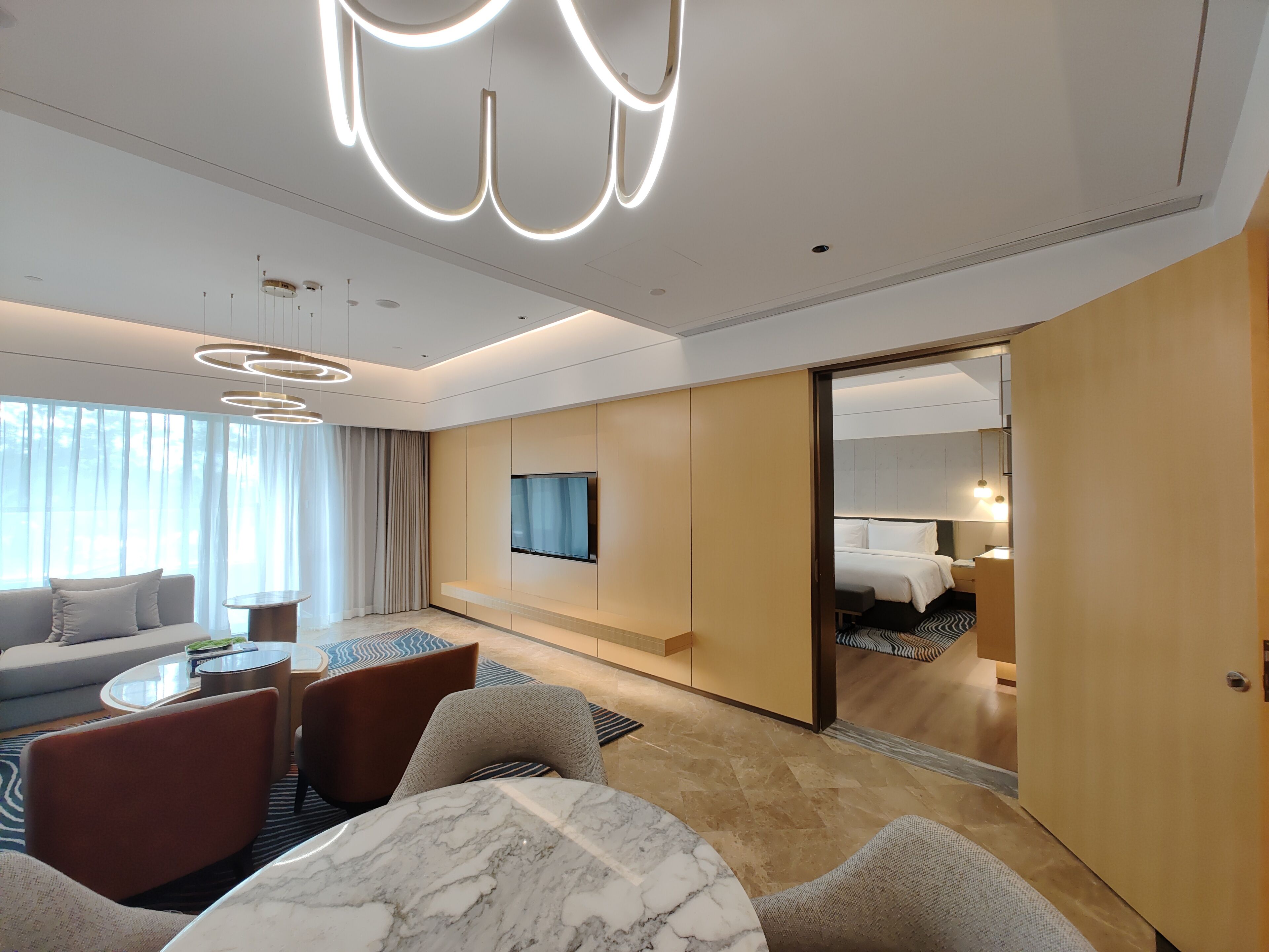 Una habitación de hotel moderna con sofá, sillones, una mesa de comedor, televisor y cama.