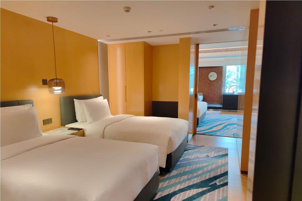 Habitación de hotel con dos camas, una mesita de noche, una lámpara de pared y un tapete estampado.