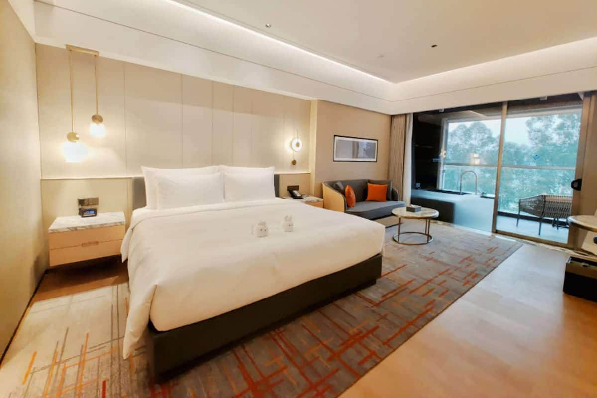 Una habitación de hotel moderna con una cama grande, mesitas de noche, un sofá y una pequeña mesa redonda.