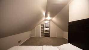 A bedroom with a bed, a closet, and a staircase leading to a loft area.