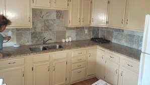 A kitchen with beige cabinets, a granite countertop, a sink, and a refrigerator.