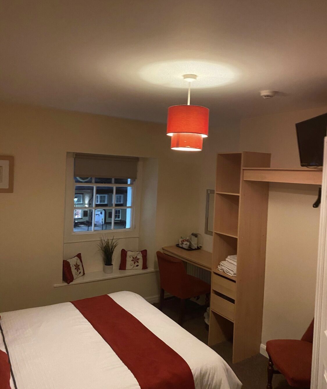 A bedroom with a bed, a desk, a chair, a window, and a wardrobe.