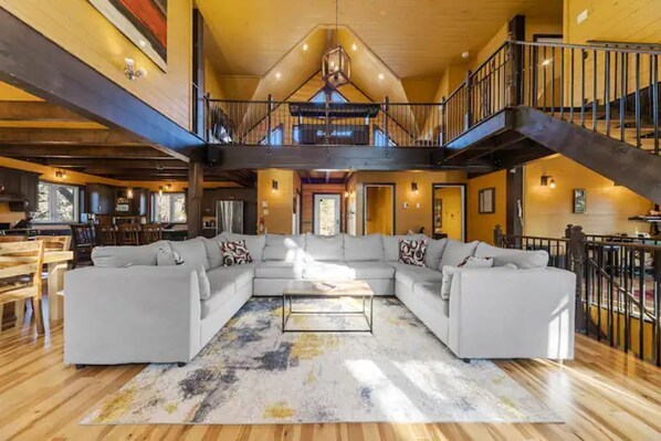 A spacious living area with a large sectional sofa, a coffee table, and a staircase leading to an upper level.