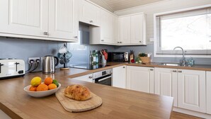 Una cocina con armarios blancos, encimera de madera, tostadora, hervidor, microondas y pileta.