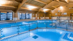 Una piscina interior con vigas de madera, ventanas de vidrio y suelo de baldosas.