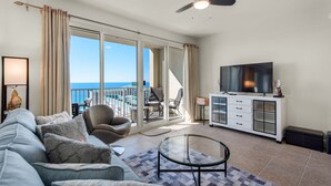 Ein geräumiges Wohnzimmer mit einer großen Couch, einem Glastisch, einem Flachbildfernseher und einem Balkon mit Meerblick.
