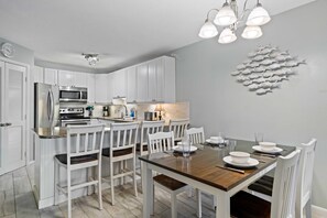 Una cocina moderna con armarios blancos, una mesa de comedor de madera y una obra de arte con motivos marinos.