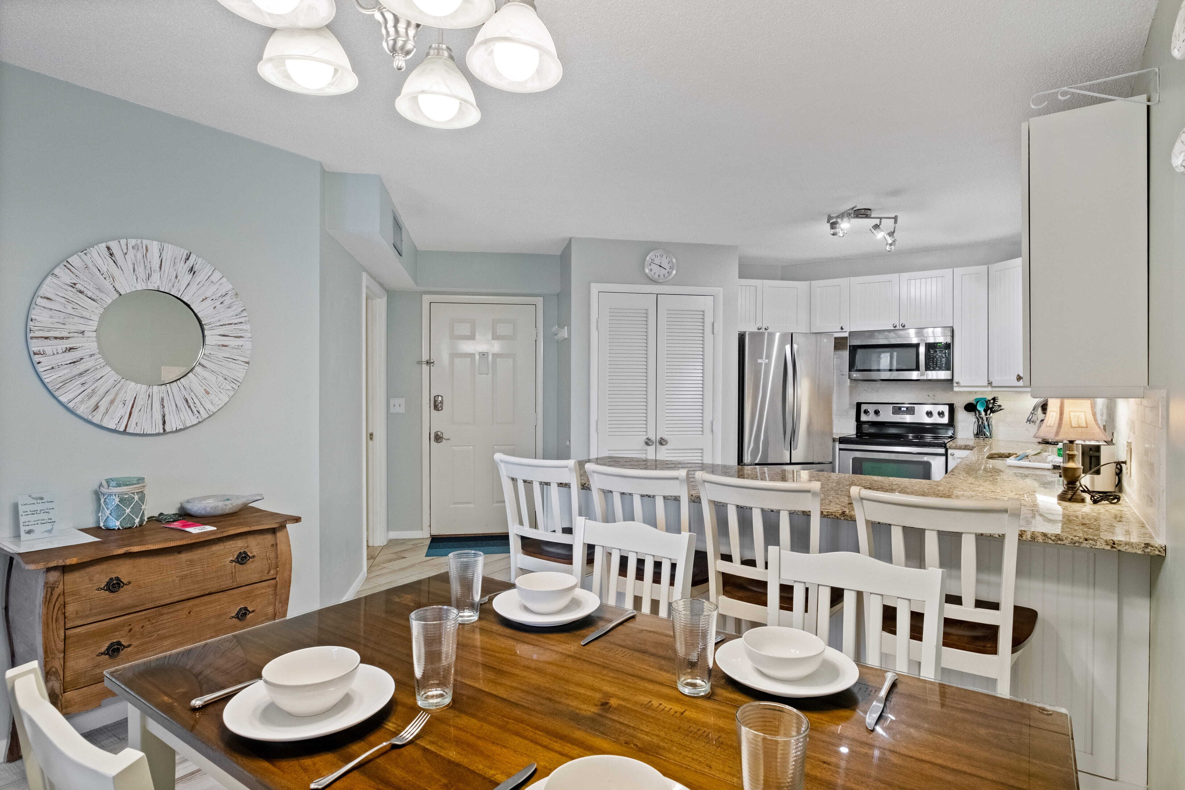 A modern kitchen with white cabinets, stainless steel appliances, and a wooden dining table set for four.