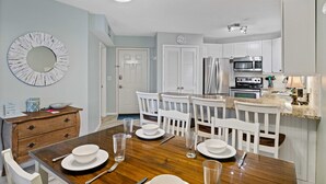 A modern kitchen with white cabinets, stainless steel appliances, and a wooden dining table set for four. - Beautiful Spacious Condo Overlooking Pool - walk to Beach and  Coligny Plaza ! (Hilton Head Island)