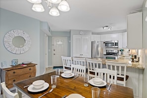 Une cuisine moderne avec des meubles blancs, des appareils en acier inoxydable et une table à manger en bois pour quatre personnes.
