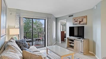 A living room with a sofa, coffee table, TV, and sliding glass doors leading to an outdoor area.