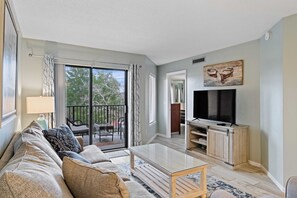 A living room with a sofa, coffee table, TV, and sliding glass doors leading to an outdoor area. - Beautiful Spacious Condo Overlooking Pool - walk to Beach and  Coligny Plaza ! (Hilton Head Island)