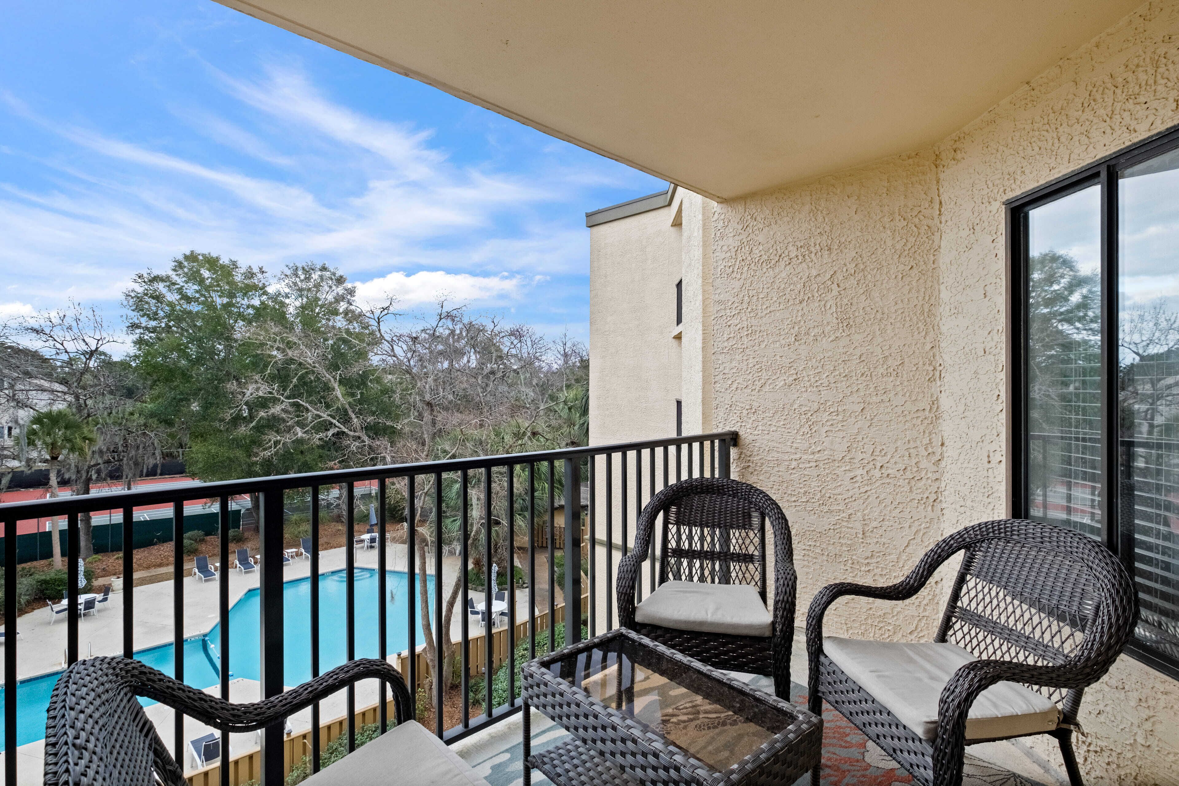 A balcony with wicker chairs and a view of a swimming pool.