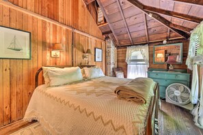 Ein Schlafzimmer in einer Holzhütte mit einem Bett, Nachttischlampen, einem Schminktisch und einem Ventilator.