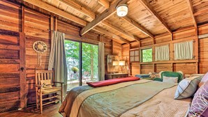 A wooden cabin bedroom with a large bed, a rocking chair, and a window overlooking greenery. - Douglas 'Whispering Winds' Cottage w/ Beach! (Douglas)