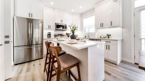 A modern kitchen with white cabinetry, stainless steel appliances, and a central island with bar stools.