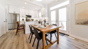 A modern kitchen with white cabinets, a wooden dining table, and a stainless steel refrigerator.