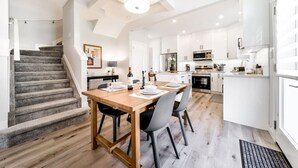 A modern kitchen with white cabinets, a dining area with a wooden table and chairs, and a staircase leading to another level.