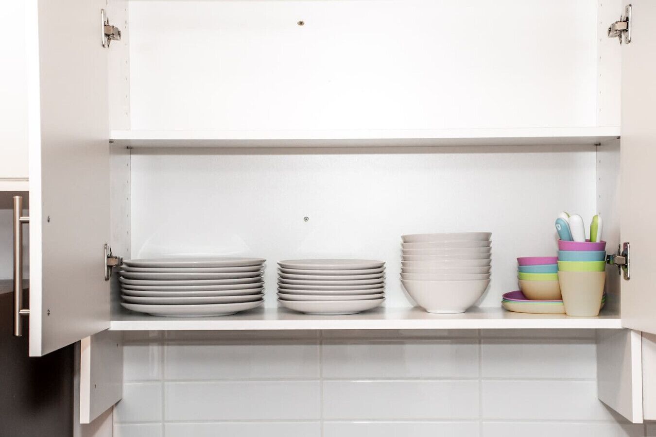 A kitchen with white cabinets, two shelves with stacked plates, and colorful bowls on the lower shelf.
