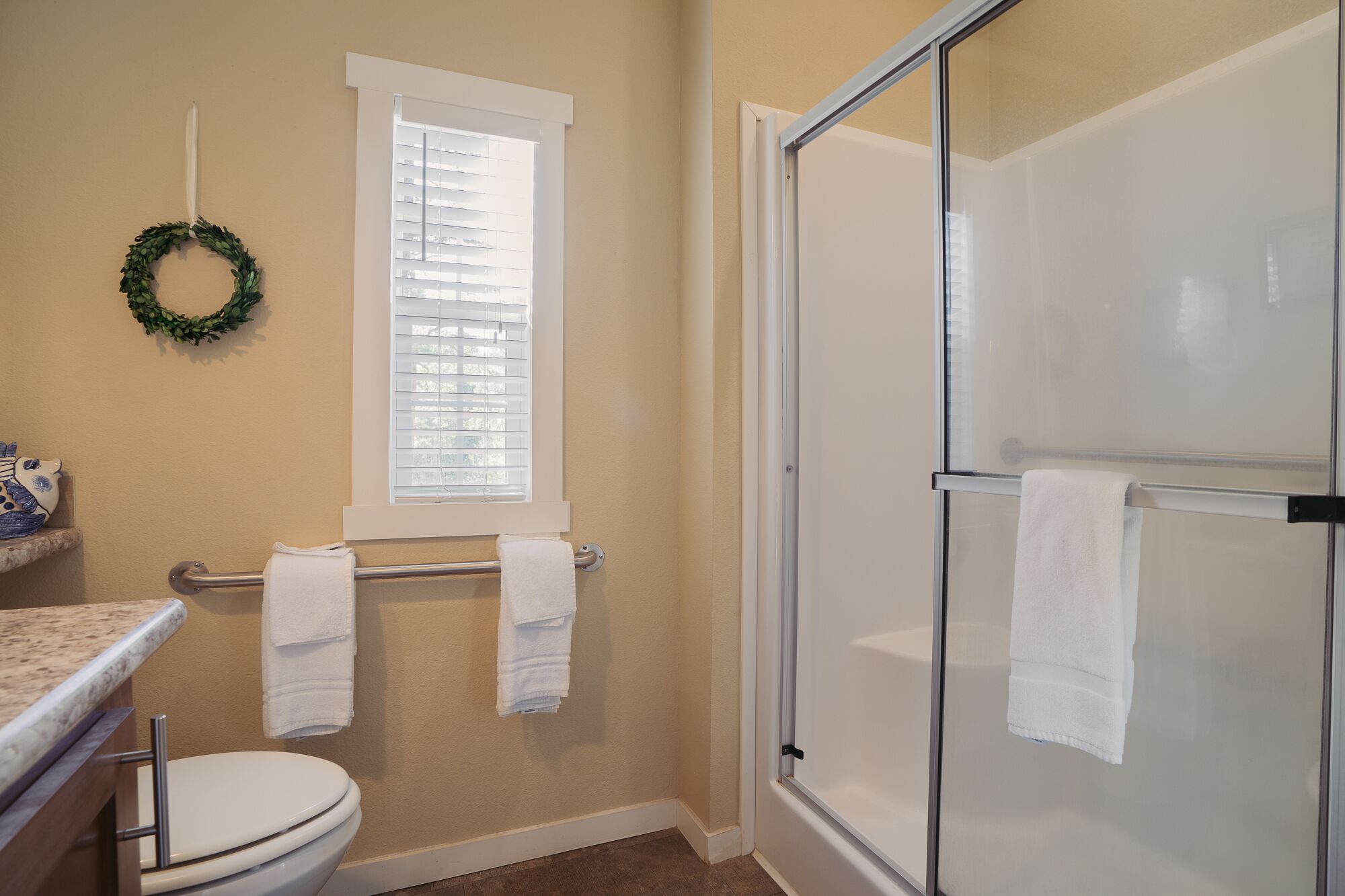 Une salle de bain comprenant des toilettes, une douche avec des portes en verre, un porte-serviettes et une fenêtre avec des stores.