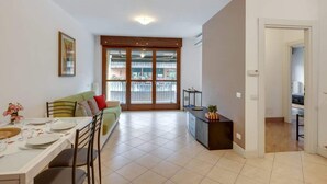 Amplia sala de estar con una mesa de comedor para cuatro, un sofá y vistas a un balcón exterior a través de puertas de vidrio.