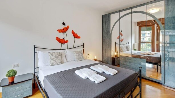 Un dormitorio moderno con una cama grande, una mesita de noche con una planta y un espejo de diseño con una original forma de arco.