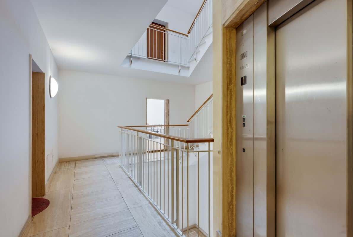 A corridor with a wooden floor, white walls, a metal railing, and an elevator.