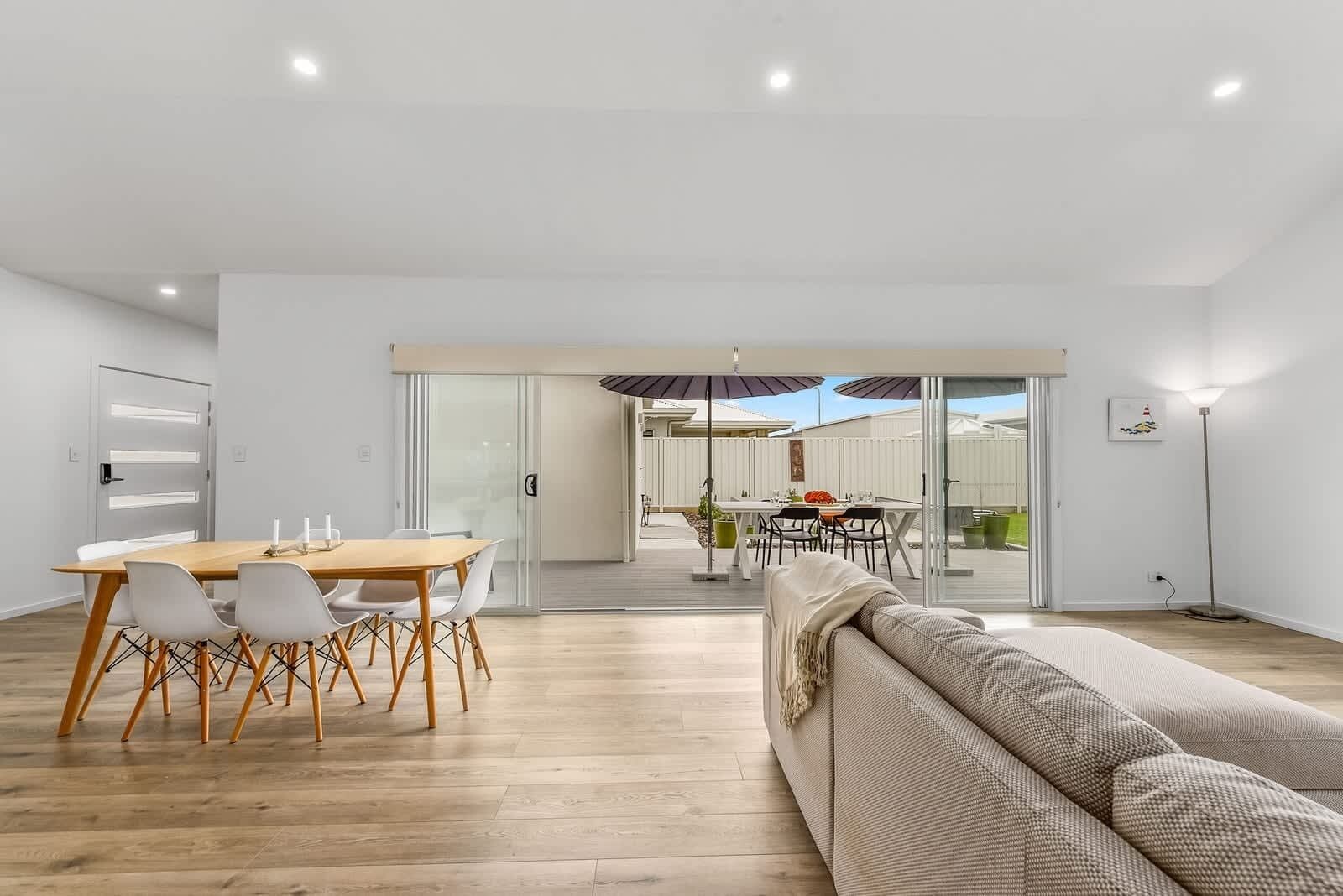 A modern interior with a dining area, a sofa, and a view through a glass door to an outdoor space.