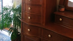 Een houten dressoir met lades en een spiegel, een houten kast met glazen deuren, en een kamerplant.
