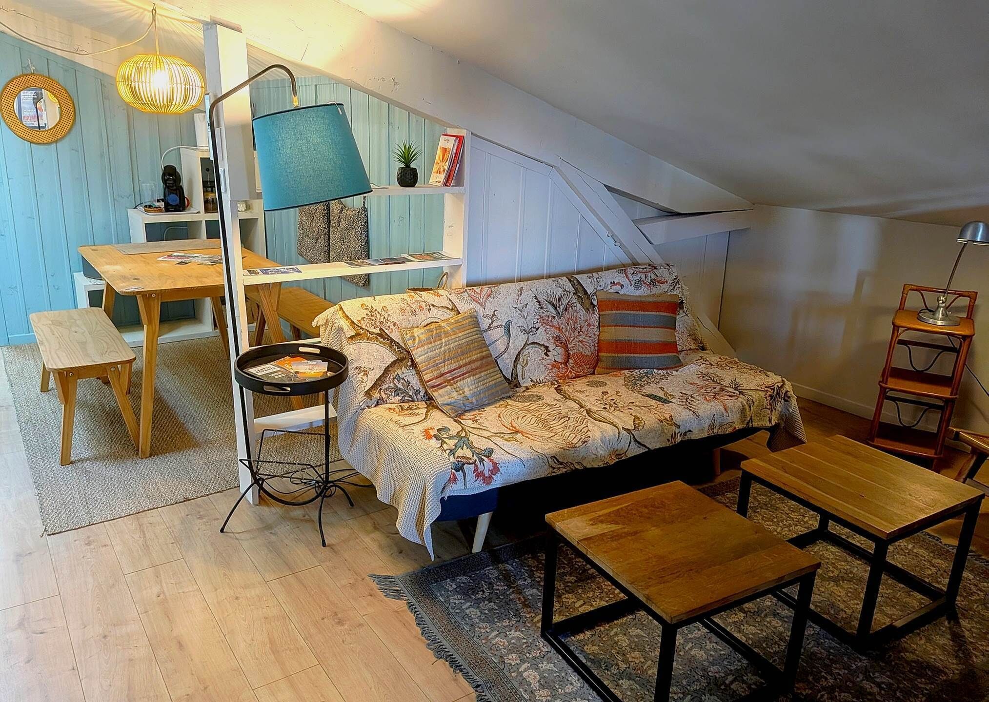A cozy loft bedroom with a sofa, a small table, a lamp, and a bookshelf.