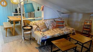 A cozy loft bedroom with a sofa, a small table, a lamp, and a bookshelf.