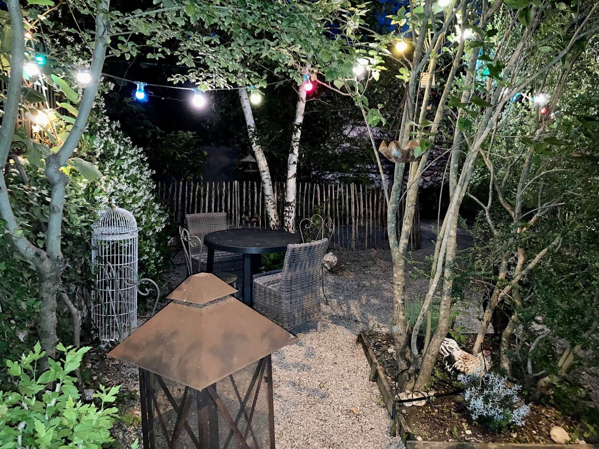 An outdoor patio area with a round table and chairs, surrounded by trees and a wooden fence.