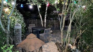 An outdoor patio area with a round table and chairs, surrounded by trees and a wooden fence.