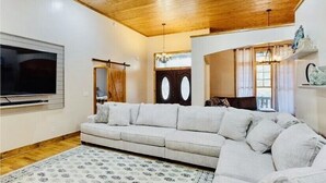 A living room with a wooden ceiling, a large flat-screen TV, a light-colored sofa, and a patterned rug. - Laurel Ridge, Privacy yet minutes from downtown, Dupont & Pisgah National Forest (Pisgah Forest)