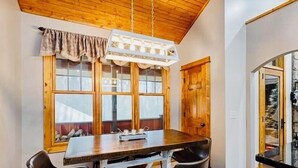 A dining area with a wooden table and chairs, a hanging light fixture, and a window with curtains. - Laurel Ridge, Privacy yet minutes from downtown, Dupont & Pisgah National Forest (Pisgah Forest)