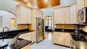 A modern kitchen with light wood cabinets, black countertops, a stainless steel refrigerator, and a black stove. - Laurel Ridge, Privacy yet minutes from downtown, Dupont & Pisgah National Forest (Pisgah Forest)