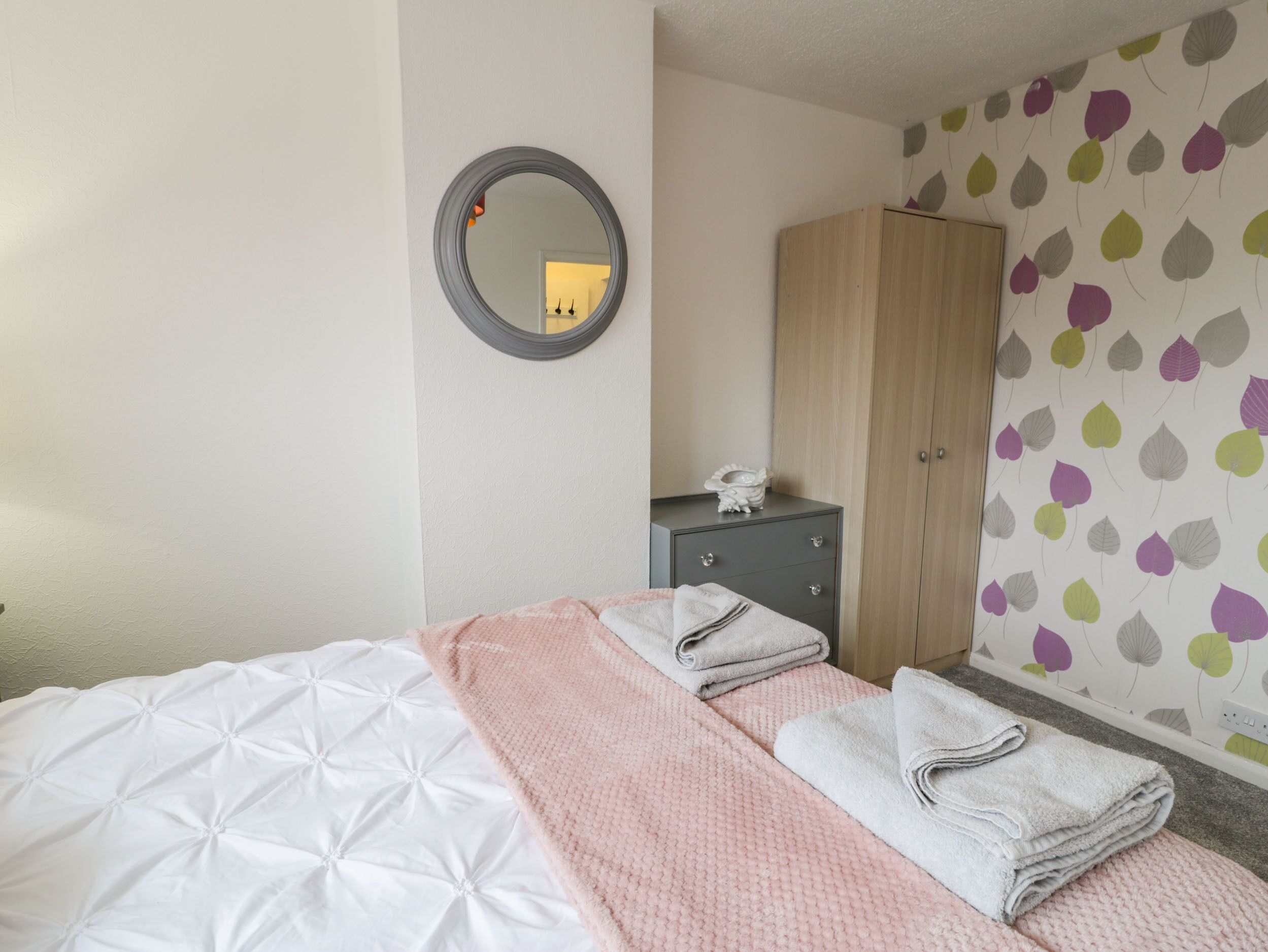 Una habitación de hotel con cama, armario, mesita de noche y espejo.