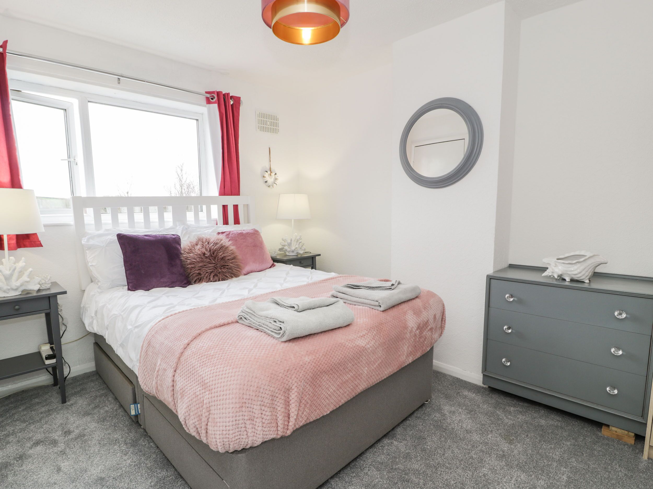 Une chambre à coucher bien rangée, avec un lit, des tables de chevet, une commode et une fenêtre avec des rideaux.