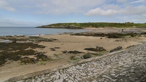 A coastal beach with rocky terrain and a stone pathway leading to the shore. - Penrallt (Cemaes Bay)