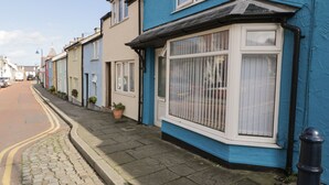 A row of terraced houses with blue and cream facades, a cobblestone street, and a clear sky. - Penrallt (Cemaes Bay)