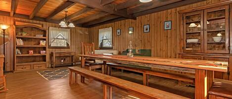 A rustic wooden interior with a long dining table, benches, and built-in shelves.