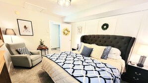 A bedroom with a large bed, a chair, a nightstand, a lamp, and a door leading to another room. - Tranquil 3 Bedroom, 2 Bath Home Near Scenic River Walk! (Baker City)