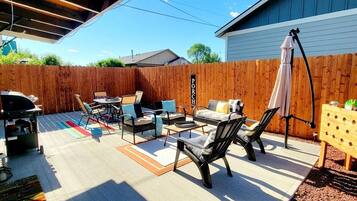 Un patio trasero con mobiliario exterior, una parrilla y una valla de madera.
