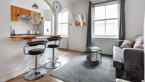 Een moderne keuken met houten kastjes, een inbouwoven en een eethoek met een barkruk.