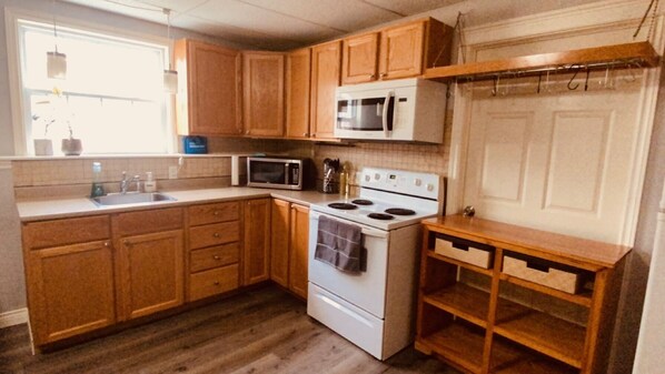 Una cocina compacta con armarios de madera, un microondas, un horno y un pequeño estante de madera.
