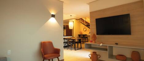 A modern living room with a flat-screen TV, a wooden accent wall, and a dining area in the background.