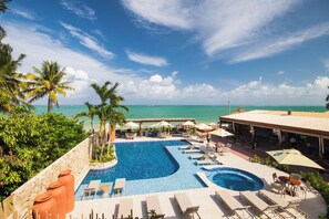 Zwembad van een resort met ligbedden en parasols, met uitzicht op een strand en de oceaan.