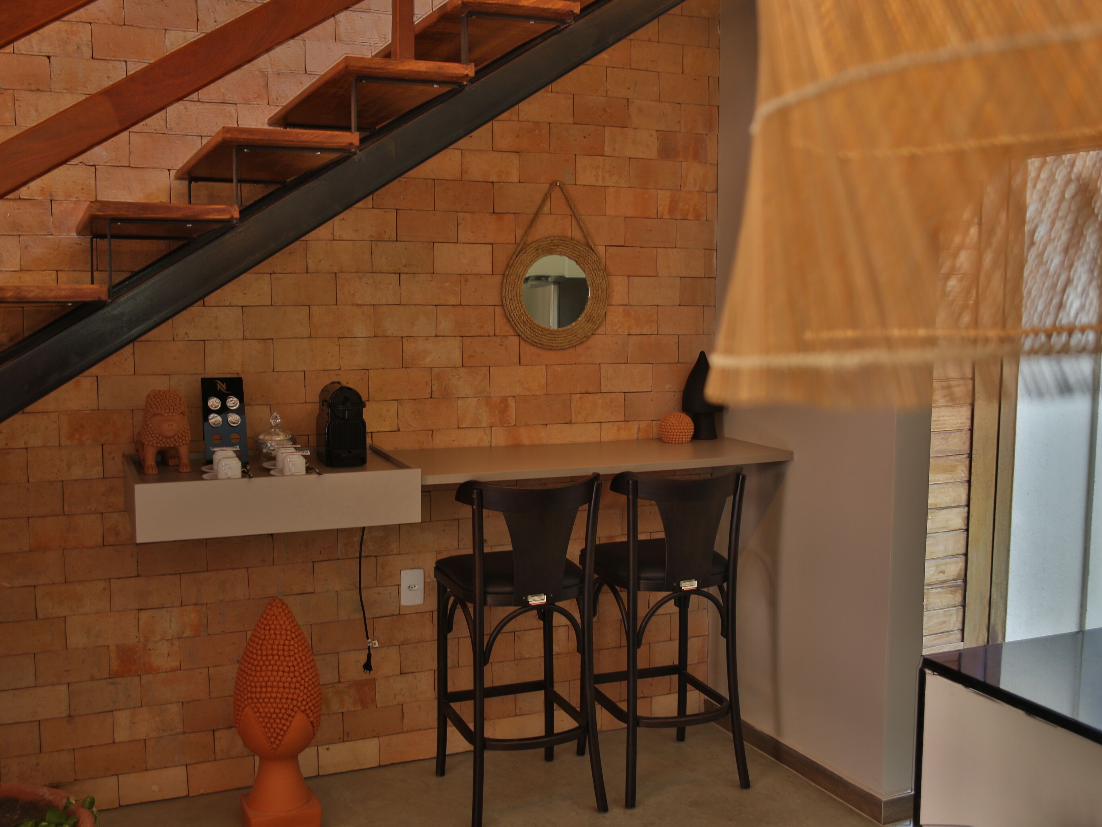 Una cocina con pared de ladrillo, escalera de madera, un espejo colgante y una pequeña mesa con sillas.