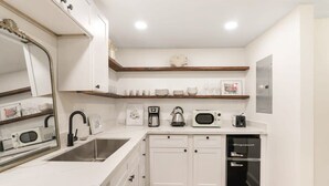 A modern kitchen with white cabinets, a stainless steel sink, a coffee maker, a kettle, a microwave, and a black refrigerator.